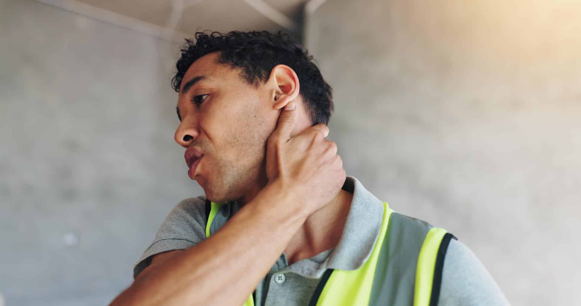 Construction worker holding his neck in pain, possibly due to cervical spondylosis or spinal degeneration.