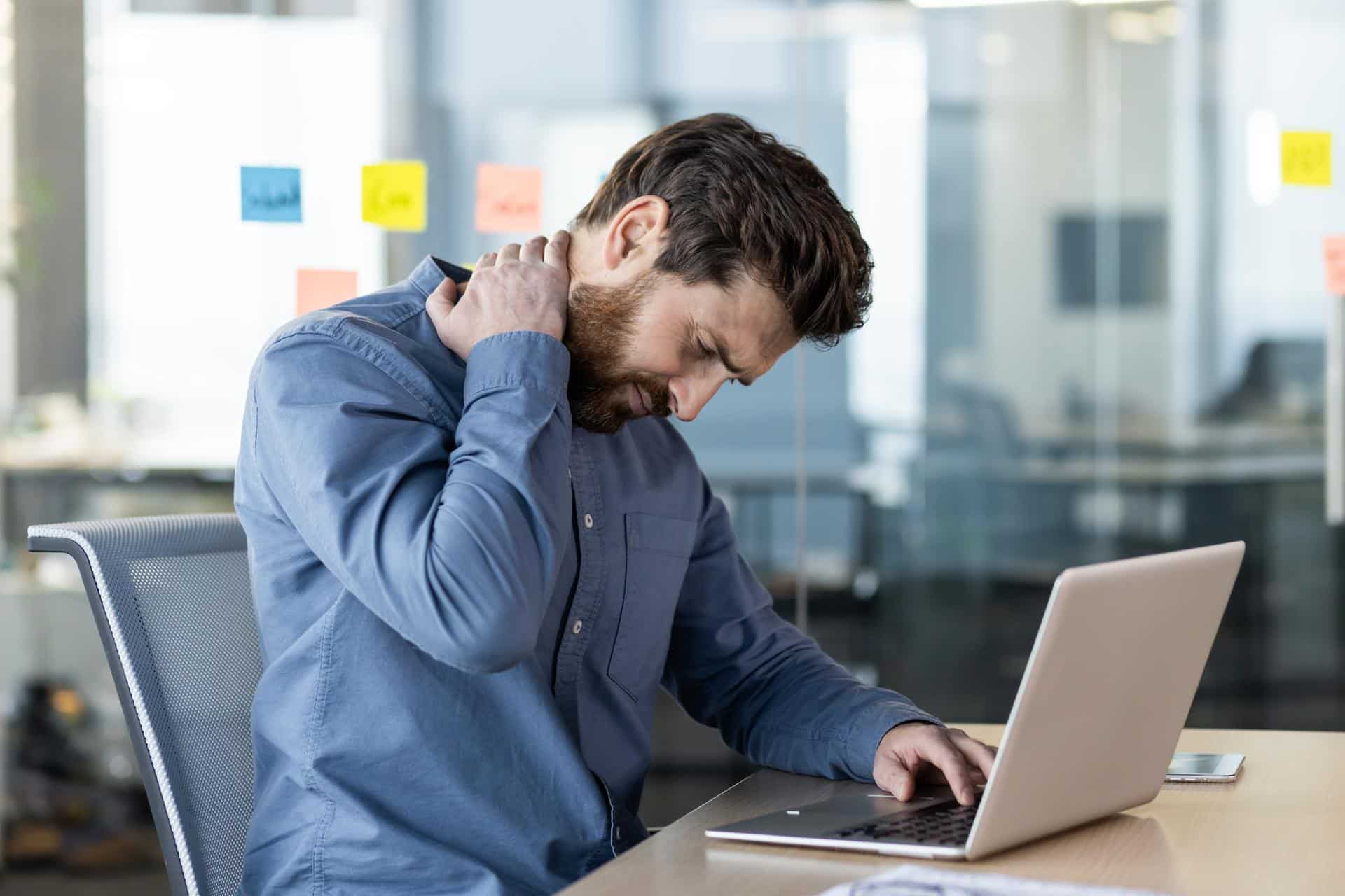 Man holding his neck in pain at his desk in Lafayette, LA office