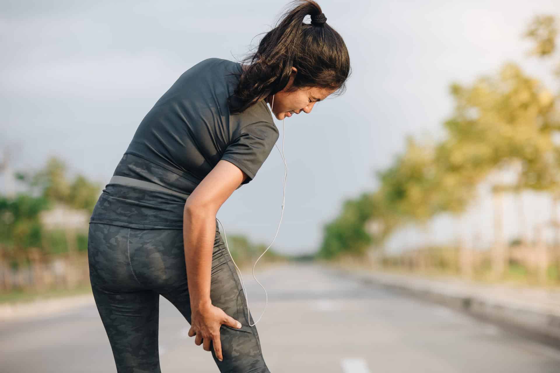 Female runner clutching her leg due to sciatic nerve pain while exercising outdoors in Lafayette, Louisiana